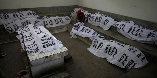 A Pakistani volunteer sits among the death bodies of people killed in a hotel fire in Karachi, Pakistan, Monday, Dec. 5, 2016