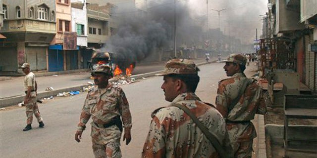 Pakistani para military troops gather near a vehicle set on fire by angry mob following the killing of a local leader of the Muttahida Quami Movement in Pakistan on Tuesday, Aug. 3, 2010. Gunmen killed dozens of people in Pakistan's largest city after the assassination of a lawmaker.