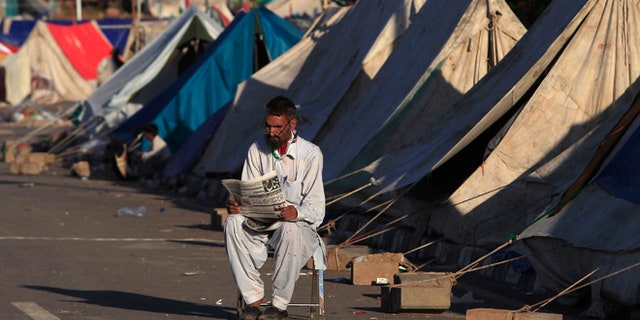 Sept. 7: An anti-government protester reads a newspaper as he sits outside makeshift tents, set up in front of the Parliament House during the Revolution March in Islamabad.