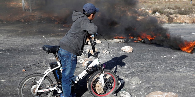 A boy stands in front of a burning barricade during a protest against U.S. President Donald Trump's decision to recognize Jerusalem as the capital of Israel, near the Jewish settlement of Beit El, near the West Bank city of Ramallah December 17, 2017.