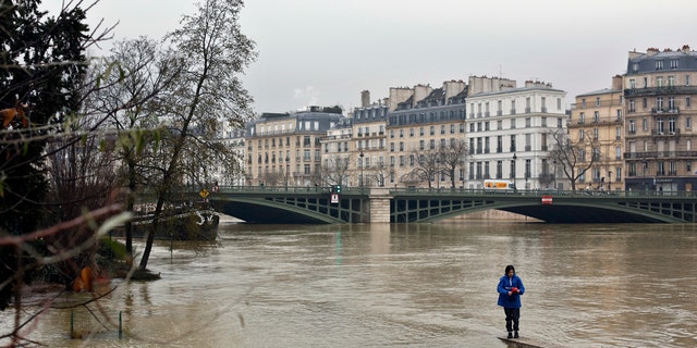 A woman walks along a low wall on the flooded banks of the river Seine in Paris, Saturday, Jan. 27, 2018.