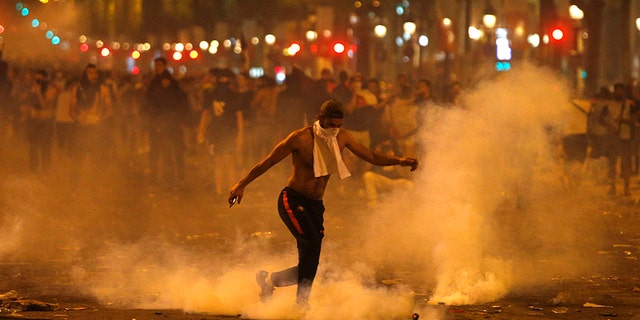 A man kicks a tear gas canister thrown by riot police during clashes on the Champs Elysees avenue where soccer fans were celebrating France's World Cup victory over Croatia.