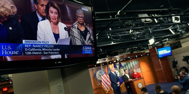 TV monitors play Pelosi's speech on the House floor while a news conference that she was scheduled to attend goes on in the background.