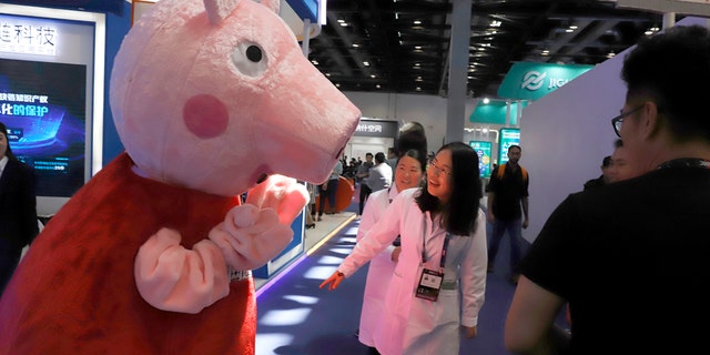 In this April 27, 2018, photo, a woman reacts to a Peppa Pig mascot during the Global Mobile Internet Conference (GMIC) in Beijing, China. 