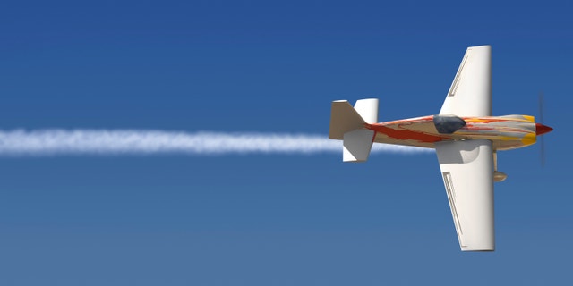 Single engine plane in the sky with a trail of smoke following it