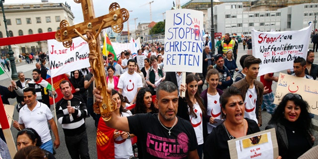 August 17, 2014: People hold crosses and signs during a rally organized by Iraqi Christians living in Germany denouncing what they say is repression by the Islamic State militant group against Christians living in Iraq, in Berlin. Some of the signs read "Stop ISIS, save the Christians" and "Stop all shipment of weapons into the Middle East.”