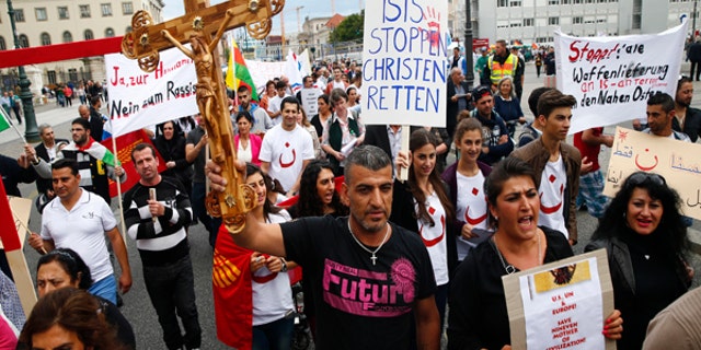 August 17, 2014: People hold crosses and signs during a rally organized by Iraqi Christians living in Germany denouncing what they say is repression by the Islamic State militant group against Christians living in Iraq, in Berlin. Some of the signs read "Stop ISIS, save the Christians" and "Stop all shipment of weapons into the Middle East.”