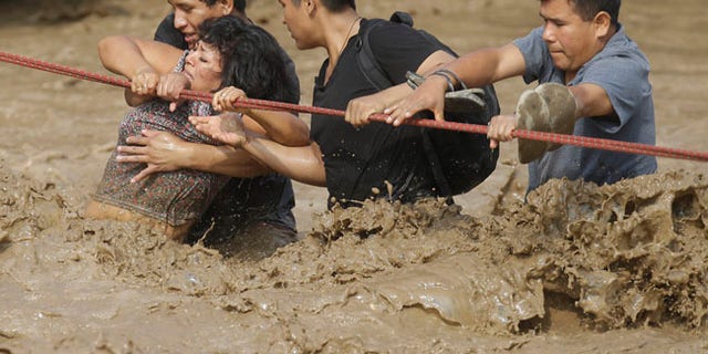 A group of people, stranded in flood waters, hold onto a rope as they wade through the water in Lima, Peru.