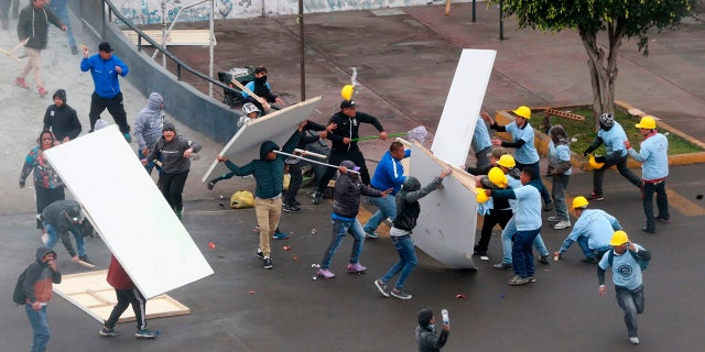 In this photo provided by the Andina government news agency, Alianza Lima club soccer fans, left, fight with members of an evangelical church, yellow helmets at right, outside the soccer club's stadium in Lima, Peru.