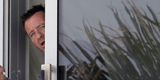 Nov. 6, 2014 file photo, Phil Rudd, drummer for the rock band AC/DC, gestures from a window at his house in Tauranga, New Zealand.