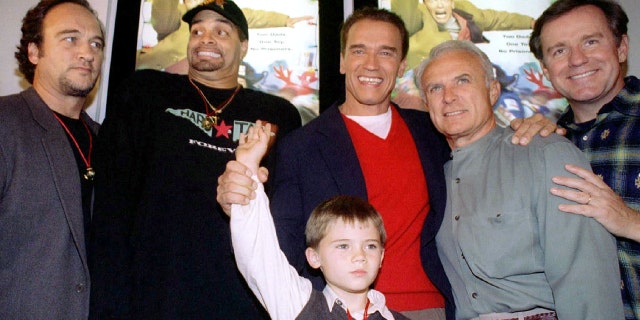 Actor Arnold Schwarzenegger, red sweater, is flanked by co-stars, from left, James Belushi, Sinbad, Robert Conrad and Phil Hartman and holds the hand of Jake Lloyd, before attending the premiere of their film, "Jingle All The Way, at the Mall of America in Bloomington, MN, November 16, 1996.