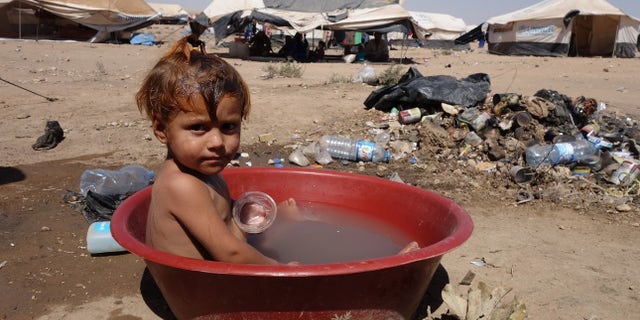 August, 2017: A child in a makeshift, polluted bath at Arisha camp in Hassakeh governorate, Syria. Around 6000 people are accommodated in the camp in very dire conditions, with no clean water, no medical services and no toilets. It was established in June 2017, and the area used to serve as an oil refinery, hence toxic waste could be found on site.