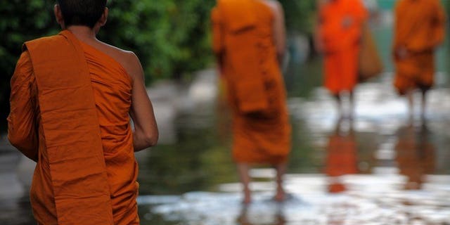 Thai Buddhist monks walk through floodwaters at a pagoda in Bangkok on October 27, 2011. Thai police said Wednesday they had arrested two monks for procuring a 14-year-old boy to perform sexual acts with an abbot, in the latest scandal to shake the kingdom's Buddhist clergy.