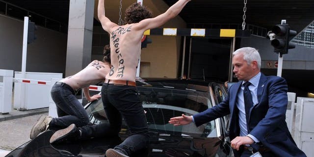Femen activists try to stop the car of Tunisian Prime Minister Ali Larayedh from leaving the EU commission building after his working session with European Commission President at the EU headquarters in Brussels on June 25, 2013. Three topless feminist activists staged a protest by jumping on the car.