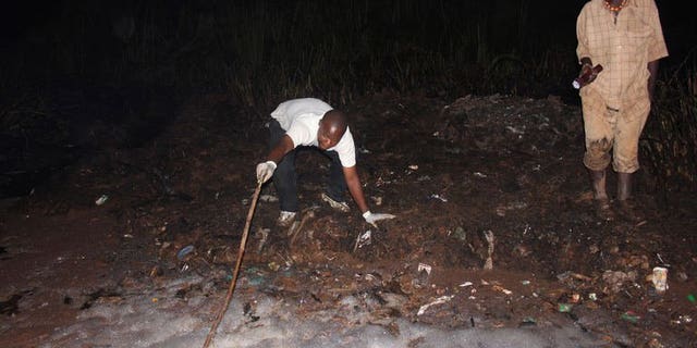 A man uses a stick to as he tries to pull out a body from a hole on June 30, 2013 in Namungoona, a Kampala suburb. At least 31 people have died in a blaze that engulfed an oil tanker after it was hit by another vehicle in a suburb of the Ugandan capital, police said Sunday.
