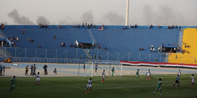 Smoke from explosions billow on the background as Iraq plays a friendly match against Liberia at al-Shaab Stadium in Baghdad on May 27, 2013. FIFA on Wednesday barred Iraq from hosting international football friendlies due to a massive surge in nationwide violence, barely three months after world football's governing body gave Baghdad the go-ahead.