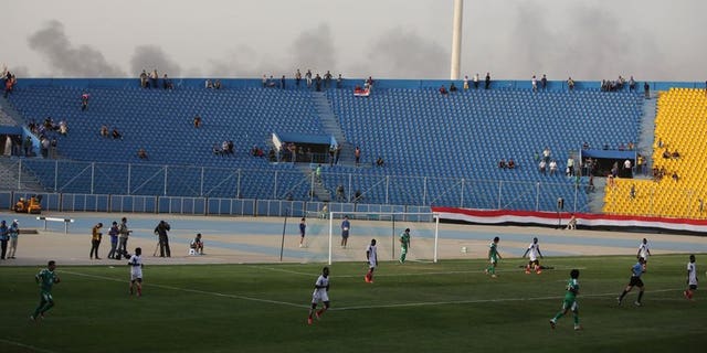 Smoke from explosions billow on the background as Iraq plays a friendly match against Liberia at al-Shaab Stadium in Baghdad on May 27, 2013. FIFA on Wednesday barred Iraq from hosting international football friendlies due to a massive surge in nationwide violence, barely three months after world football's governing body gave Baghdad the go-ahead.