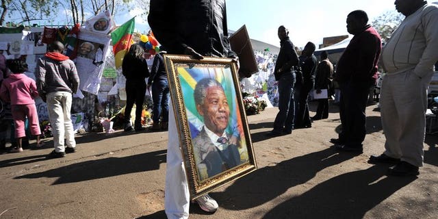 A man sells a portrait of former Nelson Mandela on Thursday outside the MediClinic Heart Hospital in Pretoria. Mandela "continues to respond to treatment" but is still in a critical condition in hospital, South Africa's presidency said Thursday.