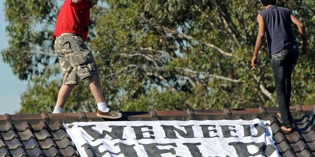 Asylum seekers (top) walk past a banner on top of a building at Sydney's Villawood Detention Centre on April 21, 2011. The UN refugee agency on Friday criticised conditions at a detention centre in Papua New Guinea where Australia sends asylum-seekers, wading into an issue looming large in Australia's forthcoming election.
