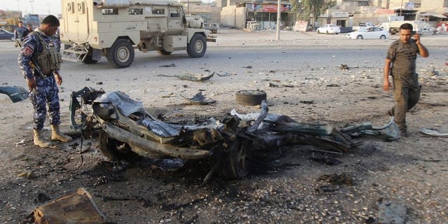 An Iraqi soldier (L) inspects the wreck of a car bomb after it exploded in the military zone of the northern Iraqi city of Kirkuk on July 11, 2013.