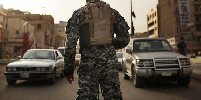 An Iraqi police officer watches cars at a checkpoint on July 20, 2011 in Baghdad. A British soldier accused of overcharging a US peace group for a security contract with the private firm he set up will be extradited to the United States, the Home Office said.