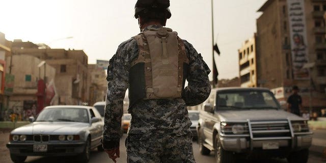 An Iraqi police officer watches cars at a checkpoint on July 20, 2011 in Baghdad. A British soldier accused of overcharging a US peace group for a security contract with the private firm he set up will be extradited to the United States, the Home Office said.