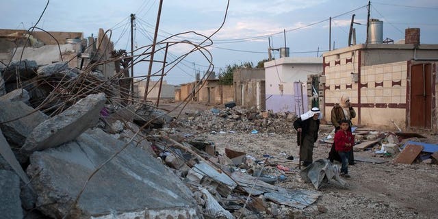Residents pass by buildings in the Syrian town of Ras al-Ain destroyed in a regime bombardment, November 26, 2012. Kurdish fighters have expelled jihadists from the flashpoint frontier town of Ras al-Ain and well as the nearby border crossing with Turkey, a watchdog said on Wednesday.