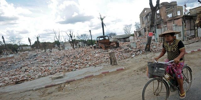 A local resident is seen riding her bicycle past the ruins of destroyed buildings in riot-hit Meiktila, central Myanmar, on June 4, 2013. Myanmar has lifted a state of emergency imposed in the riot-hit area in March where dozens of people were killed in religious violence.