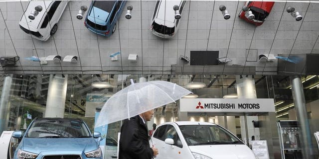 A man holding an umbrella walks past a showroom of Mitsubishi Motors Corp. in Tokyo on April 27, 2010. Mitsubishi Motors recalled more than 650,000 small cars sold in Japan over a possible fire risk.