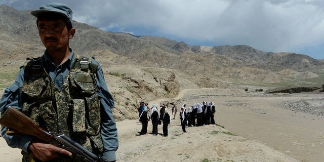A policeman stands guard as schoolgirls wait for a bus in Qara Zaghan village in Baghlan province. Two Afghan civilians were killed and several injured following two failed assassination attempts by the Taliban which targeted a provincial governor and a police chief, officials said Saturday.
