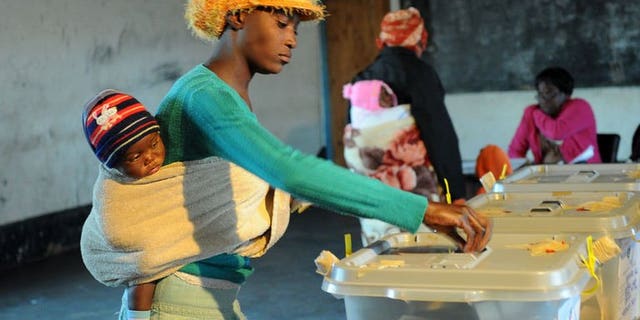 A Zimbabwean mother holding her child casts her ballot at a polling station on July 31, 2013 in Domboshava, 60km north of Harare. The first official results from Zimbabwe's disputed national assembly elections showed President Robert Mugabe's party gaining an early and overwhelming lead Thursday.