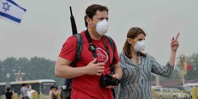 Two tourists wear face masks as they visit Tiananmen Square on a heavily polluted day in Beijing on May 8, 2013. The number of tourists visiting Beijing fell by more than 14% in the first half of this year compared to 2012, with air pollution blamed for the decline.