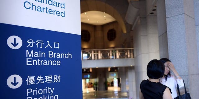 Two women inside a Standard Chartered bank branch in Hong Kong Tuesday. Standard Chartered on Tuesday said its first-half net profit fell 24 percent, with some of its businesses in emerging Asian markets seeing slower growth.