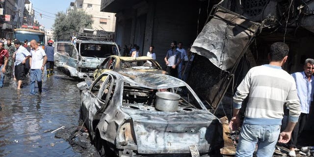 Syrians walk past a burned-out car after an attack on July 25, 2013 in the Jaramana suburb in southeast Damascus. A bomb killed 10 people in Jaramana on Tuesday, the latest in spate of blasts to hit the mainly Christian and Druze district, state television said.
