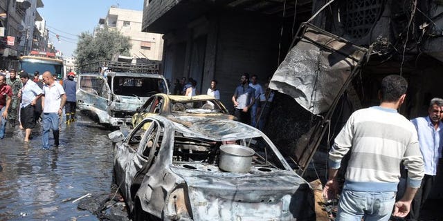 Syrians walk past a burned-out car after an attack on July 25, 2013 in the Jaramana suburb in southeast Damascus. A bomb killed 10 people in Jaramana on Tuesday, the latest in spate of blasts to hit the mainly Christian and Druze district, state television said.