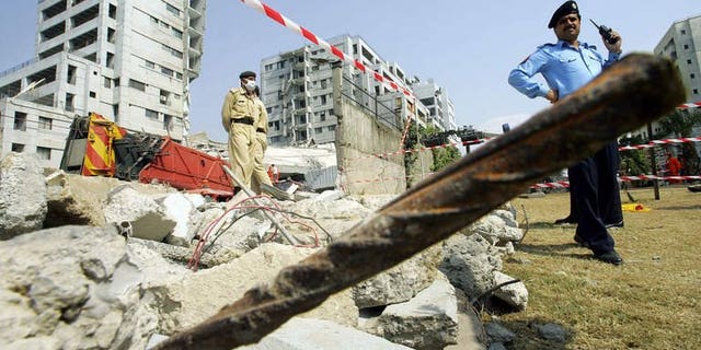Pakistani police stand guard around the Margalla Towers while rescue workers continue to look for survivors after the building collpased after a powerful earthquake rattled Islamabad, on October 11 2005. A British architect of Pakistani origin -- who is wanted over the 2005 collapse of the Margalla Towers that killed 78 people -- has been arrested in Greece.