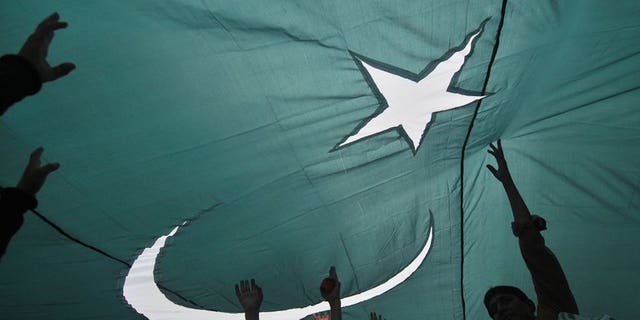 Youths gather under a giant national flag in Lahore on August 13, 2013, one day ahead of the country's Independence Day. At least one person was killed and more than 30 wounded in Karachi on Wednesday as hundreds of people fired guns in the air to celebrate Pakistan's Independence Day.