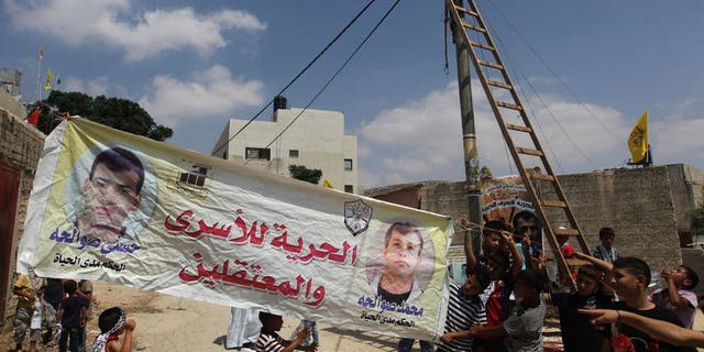 Relatives and friends of Palestinian prisoners raise a banner in the West Bank village of Azmut, east of the northern city of Nablus on August 12, 2013. Israel warned on Wednesday that it might shun a key EU research programme unless a compromise is found over the bloc's guidelines which bar funding to Jewish settlement entities.