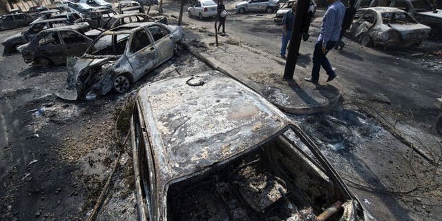 Egyptians pass by burnt vehicles outside the destroyed camp of ousted Mohammed Morsi supporters outside Rabaa al-Adawiya mosque on August 15, 2013 in Cairo, Egypt.