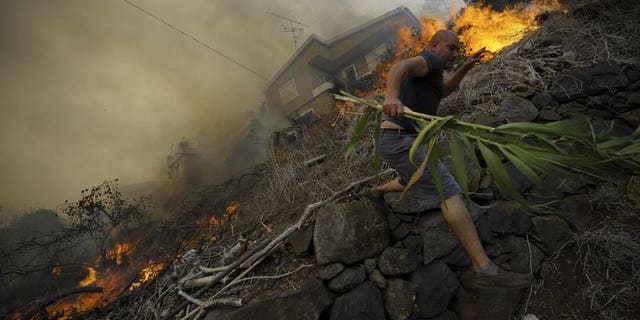 A man runs away from the flames as a wildfire rages near houses in Assomada, Madeira on July 21, 2012. A raging wildfire has prompted the evacuation of a hospital outside Funchal, capital of the Portuguese island of Madeira, officials said Saturday.