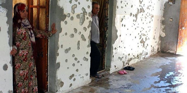 A man and a woman stand next to a wall riddled with bullets in the courtyard of a house in the Syrian town of Ras al-Ain on August 3, 2013. Al-Qaeda loyalists attacked a mainly Kurdish town in northeastern Syria sparking fighting in which 17 people were killed, two of them ambulance crew, a watchdog said on Saturday.