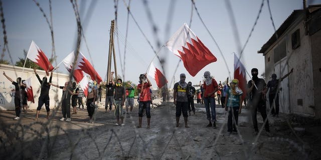 Bahraini protestors wave their national flag as they stand behind barbed wire placed by riot police during demonstration against the ruling regime in the village of Shakhora, west of Manama, on August 14, 2013. Five Bahraini police were wounded late on Saturday, as security forces clashed with opposition protesters in a Shiite village north of the capital, police said.