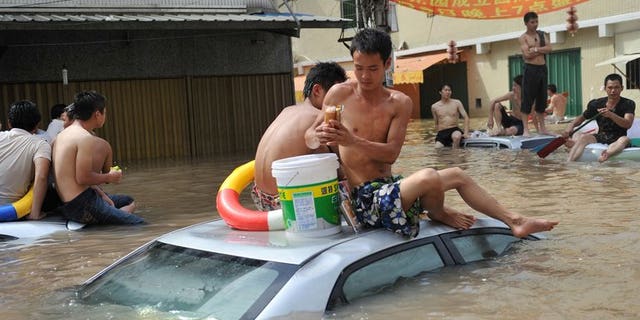 Residents sit on top of vehicles submerged by water in the flood-hit Chaonan district of Shantou, in southern China's Guangdong province, August 19, 2013. Heavy rains killed 21 construction workers as flooding spread to northwest China, state media said Wednesday, after severe weather in other parts of the country left more than 130 dead.