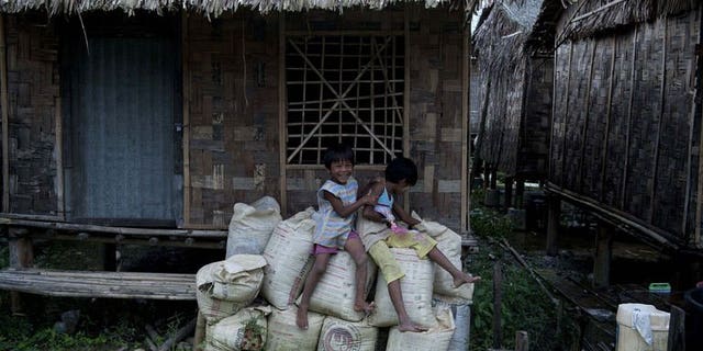 Children sit outside their bamboo house built in the compound of a Buddhist monastery and meditation center sheltering hundreds of displaced families in a suburb of Myanmar's former capital Yangon on July 19, 2013.