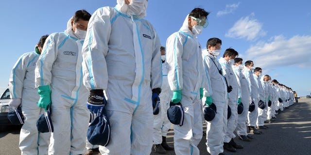 Police officers in radiation protection suits bow their heads to offer prayers in silence for tsunami victims in Namie, near the striken TEPCO's Fukushima Dai-ichi nuclear plant in Fukushima prefecture on March 11, 2013. A magnitude 5.3 earthquake rocked Japan's Fukushima prefecture early Friday morning, US seismologists said, but no tsunami warning was issued.
