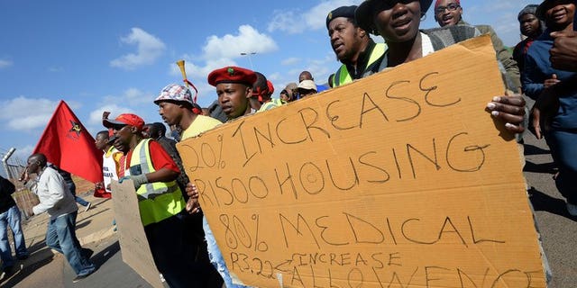 Workers on strike hold a placard asking for wage increases as they demonstrate outside Ford's plant in Pretoria on August 20, 2013.