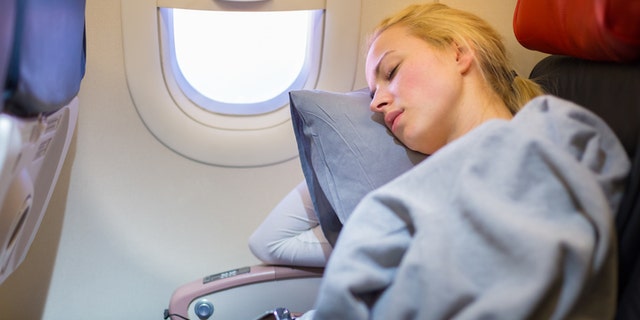 Tired blonde casual caucasian lady napping on uncomfortable seat while traveling by airplane. Commercial transportation by planes.