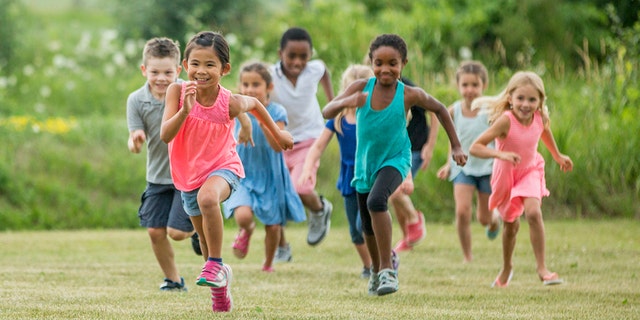 A multi-ethnic group of elementary age children are playing together outside at recess. They are chasing each other and are playing tag.