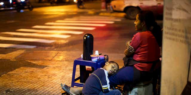 A child sleeps on the legs of his mother, who sells coffee in downtown Caracas, on March 4, 2014.