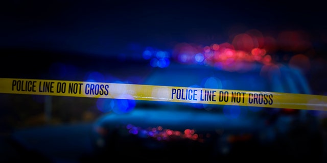 A stock photo of a Police Line "Do Not Cross" caution tape with a defocused police car with sirens flashing red and blue.